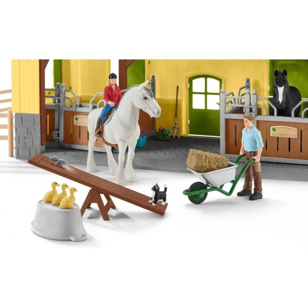 Una scena di fattoria giocattolo: Un cavaliere su un cavallo bianco, un uomo con una carriola, un'altalena con animali e un cavallo nero in una stalla.