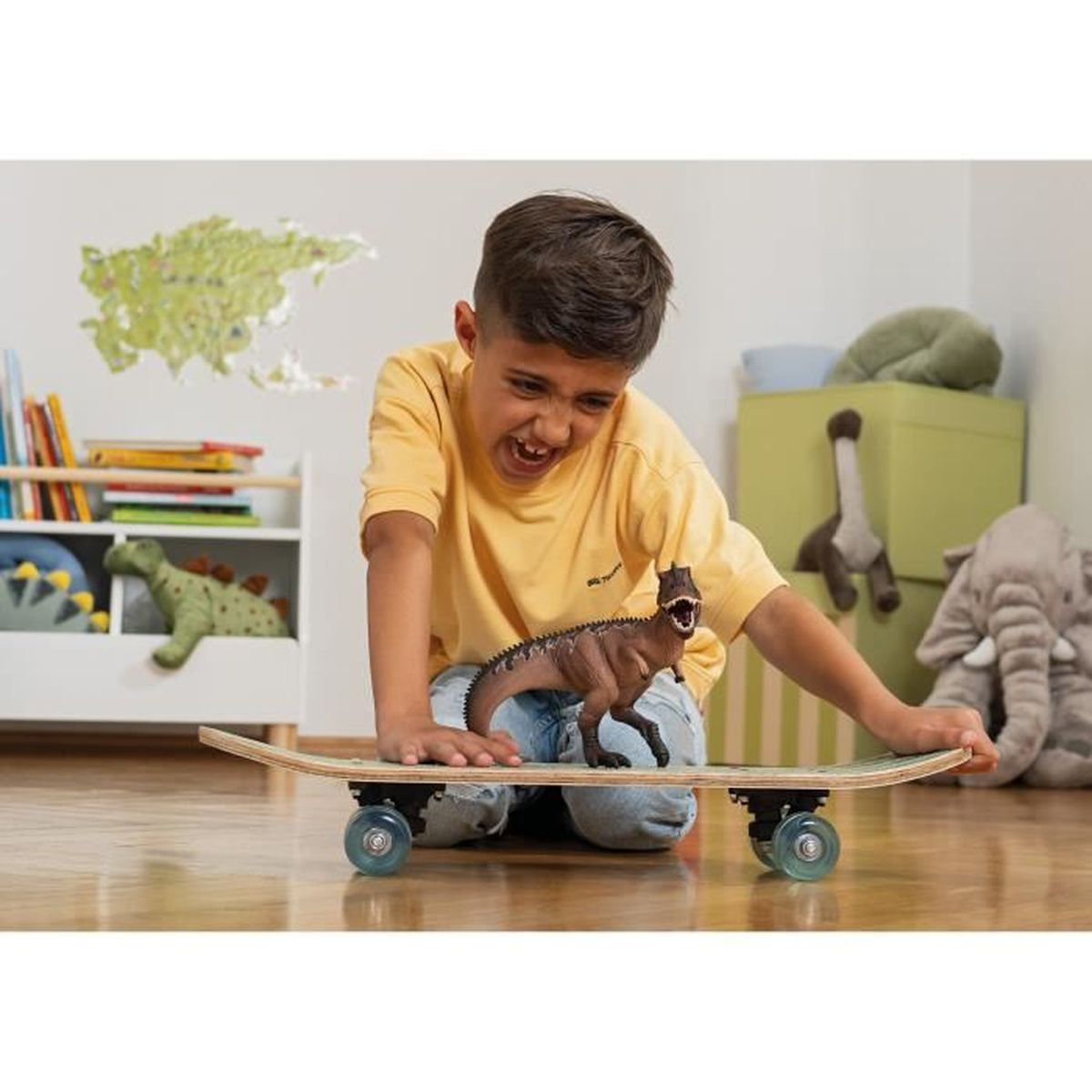 Un ragazzo è in ginocchio, sorridente, con un dinosauro giocattolo su uno skateboard. Giocattoli e una mappa sullo sfondo.