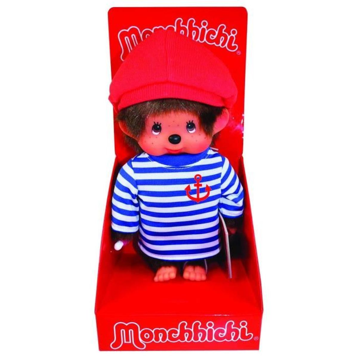 Lalka Monchhichi w czerwonym pudełku. Nosi czerwony kapelusz, niebiesko-białą koszulę w paski z kotwicą, ma brązowe futro i smoczek.