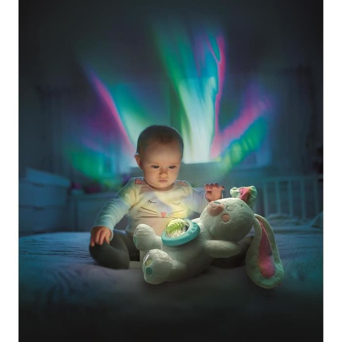 Un bambino seduto su un letto guarda un coniglietto di peluche. Luci colorate proiettate sul muro. Il bambino indossa una camicia chiara.