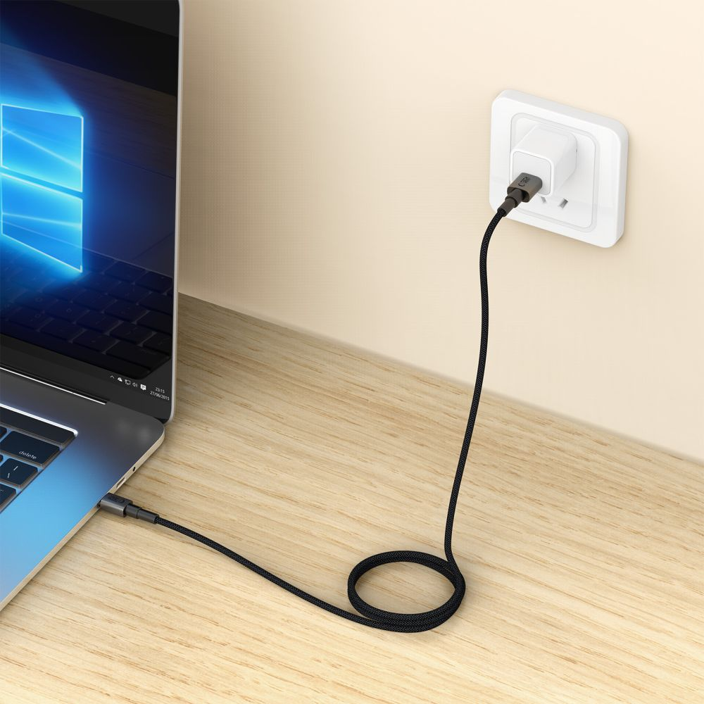Ein Laptop ist über ein schwarzes Ladekabel mit einer Steckdose verbunden. Der Laptop steht auf einem Holzschreibtisch.