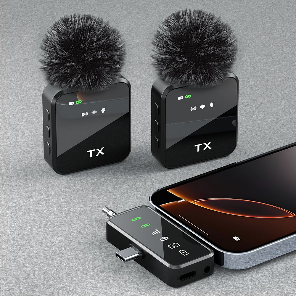 Zwei schwarze Funkmikrofone mit Fellaufsätzen, ein USB-C-Adapter und ein Smartphone auf grauem Untergrund.