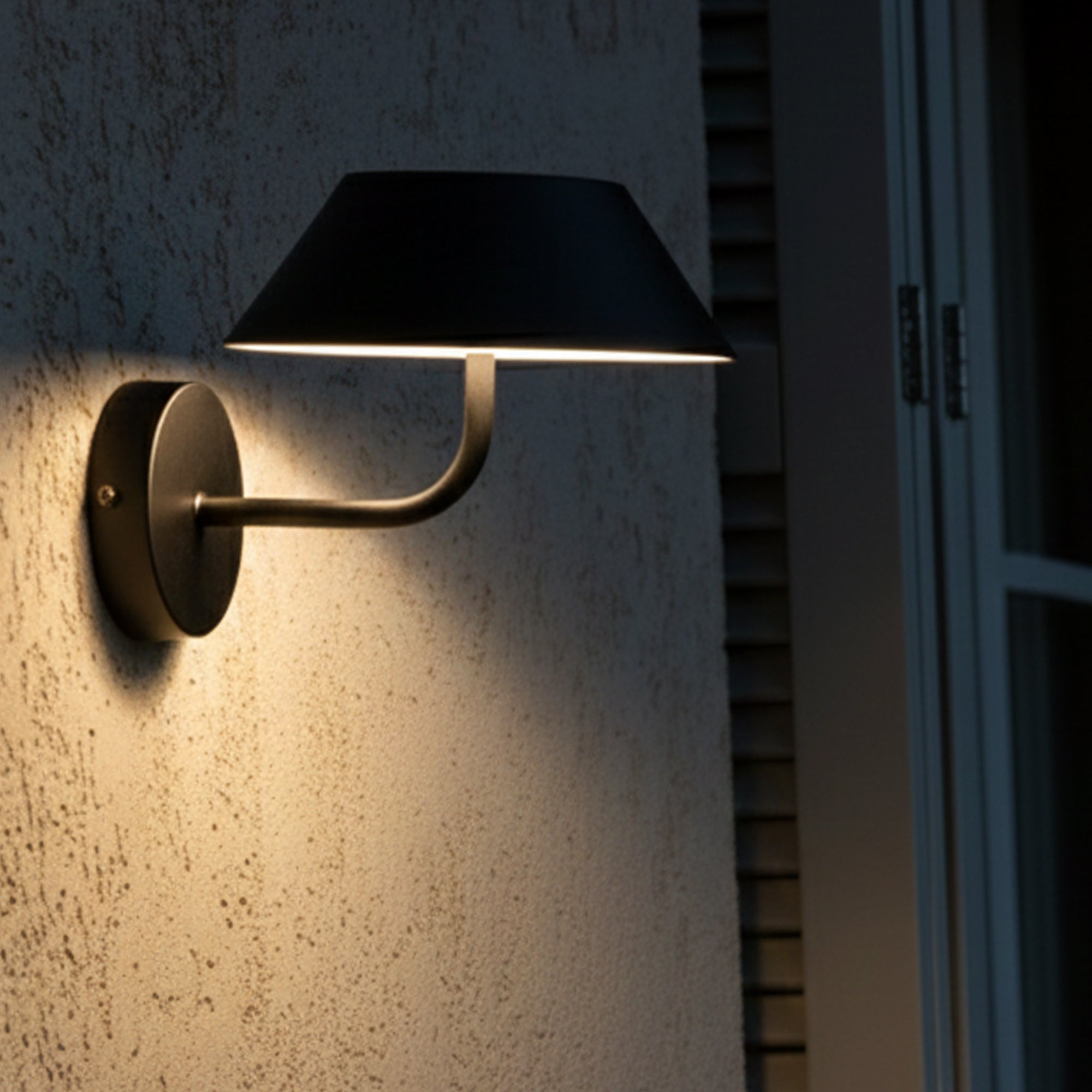 Eine schwarze Außenwandleuchte ist an einer strukturierten Wand montiert. Die Lampe hat einen gebogenen Arm und einen Lampenschirm.