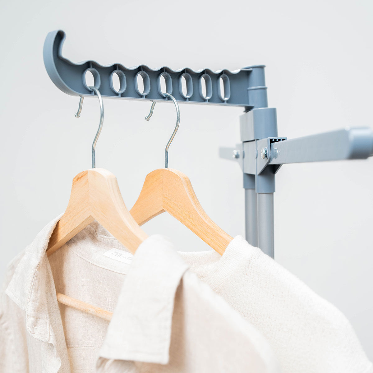 Kleidung auf Holzkleiderbügeln hängt an einem grauen Wäscheständer. Hemden und ein Pullover sind sichtbar.