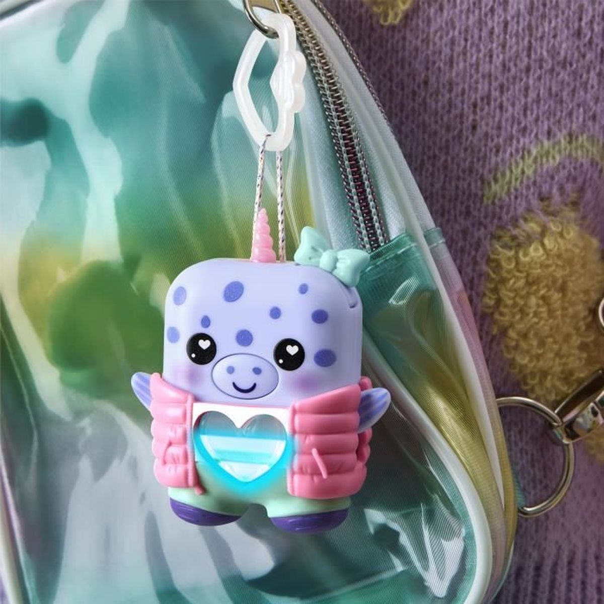 Ein Walross-Schlüsselanhänger mit rosa Weste hängt an einer Tasche. Das Walross ist lila mit blauen Punkten. Der Hintergrund umfasst einen lila Pullover.
