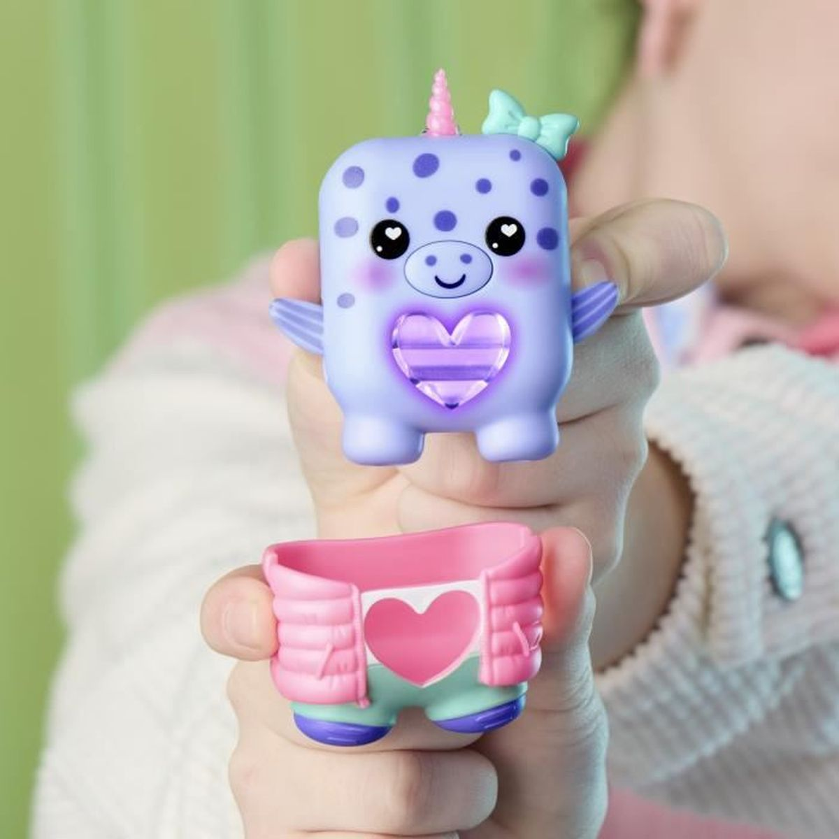 Ein Kind hält ein lila Spielzeug-Narwal mit rosa Horn und einem rosa Outfit mit Herz.