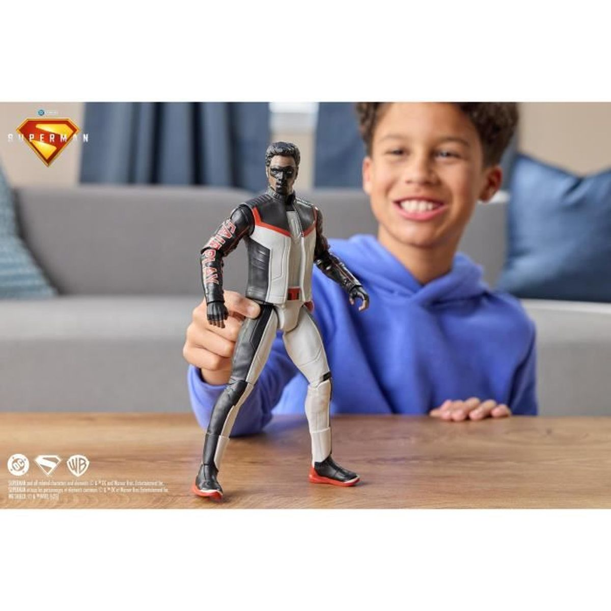 Ein Junge hält eine Superman-Actionfigur. Die Figur ist schwarz, weiß und rot. Der Junge lächelt und trägt einen blauen Hoodie.