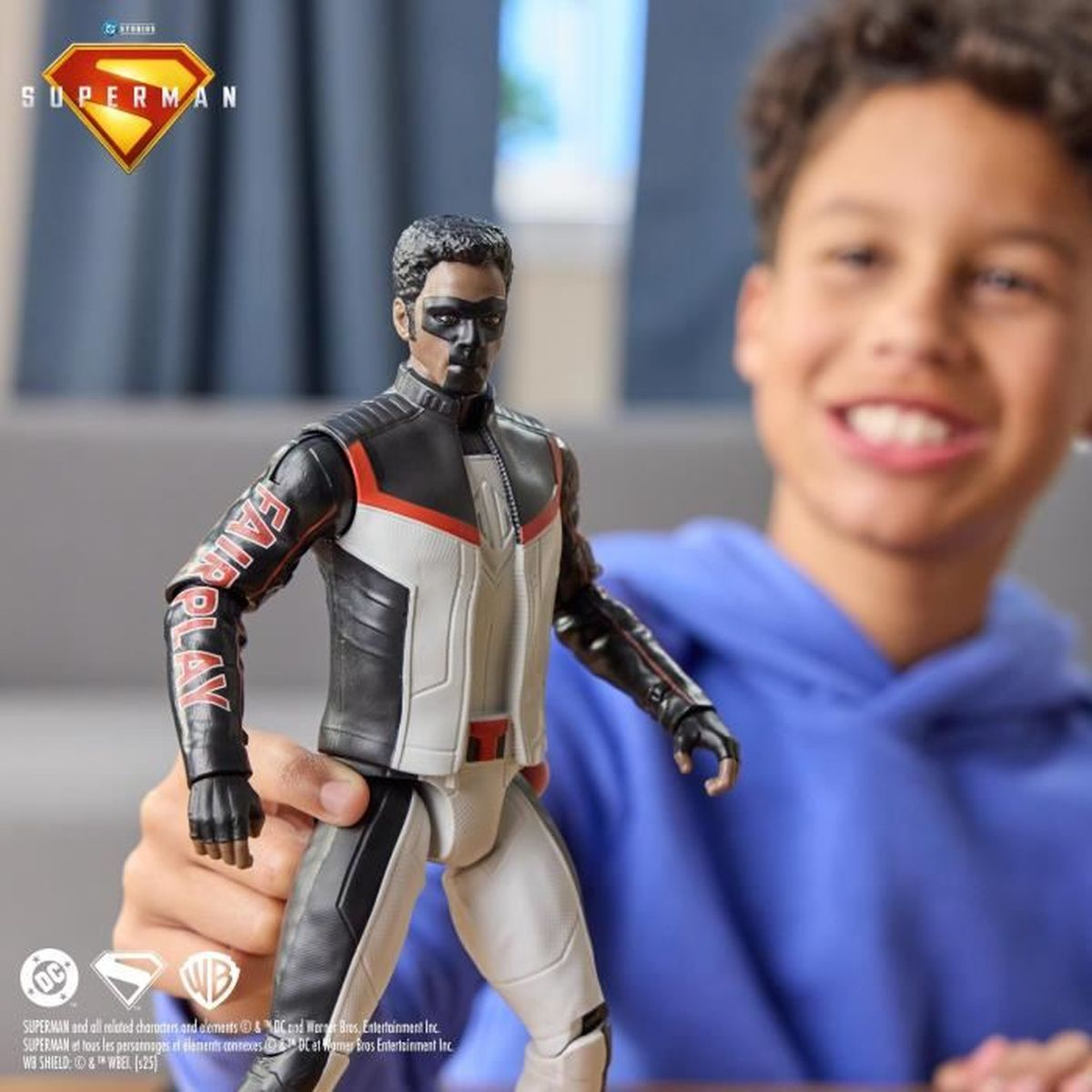 Ein Kind hält eine Fair Play Superman Actionfigur. Die Figur hat schwarz-weiße Kleidung, und im Hintergrund ist ein lächelndes Kind.