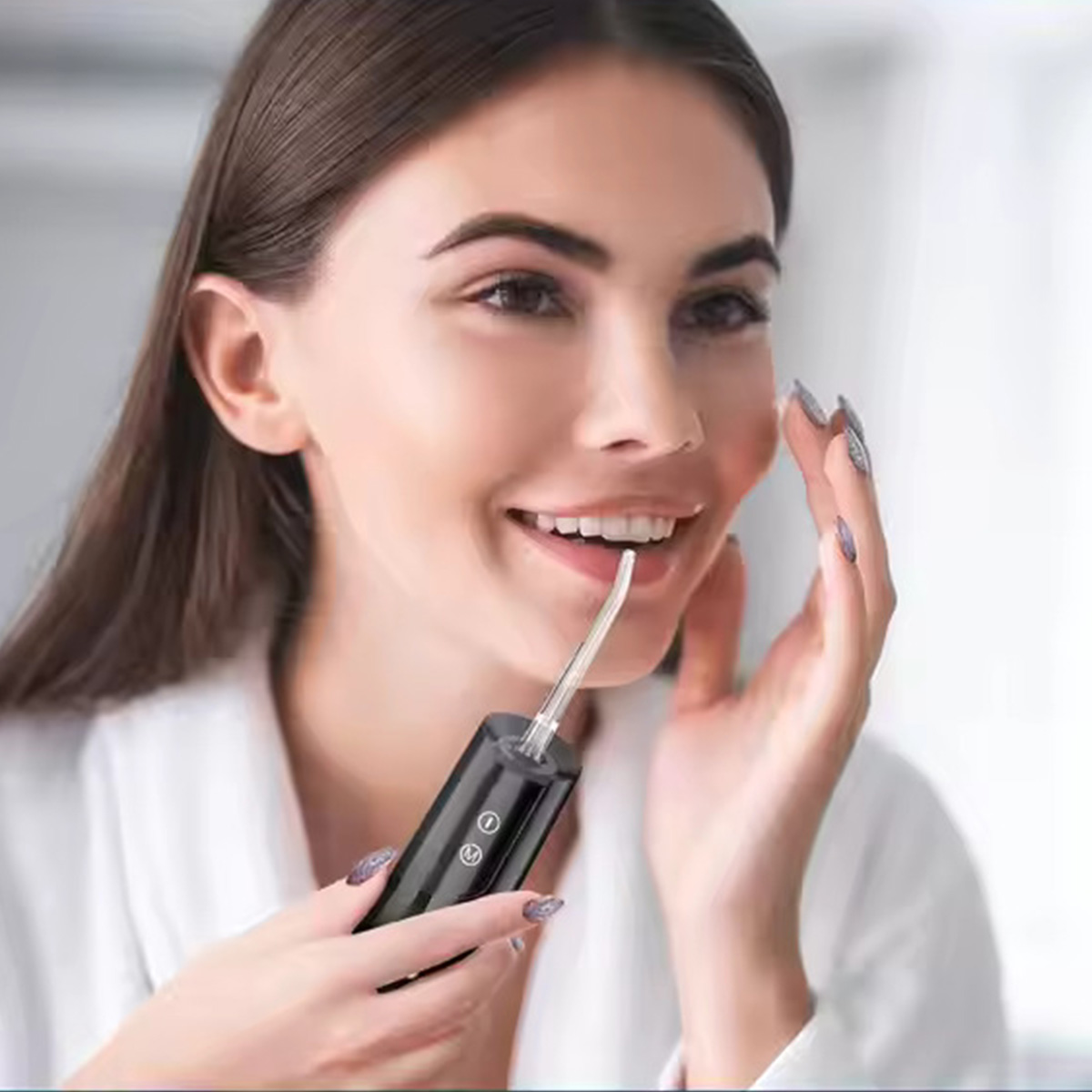 Kobieta uśmiecha się podczas używania irygatora do zębów. Trzyma irygator w jednej ręce, a drugą dotyka policzka.