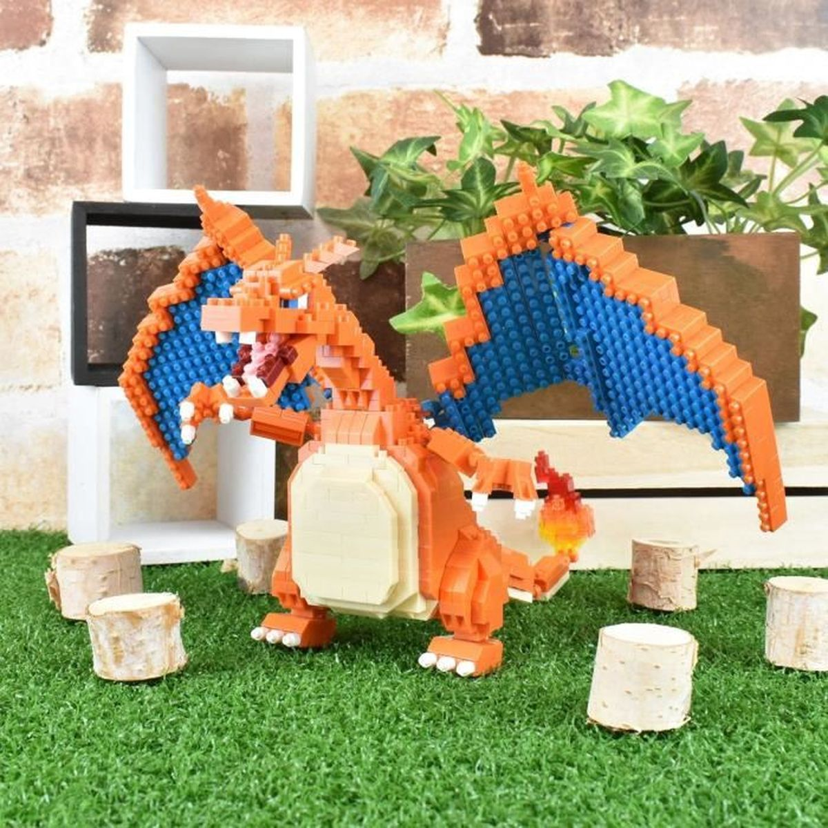 Eine orangefarbene Charizard-Lego-Figur mit blauen Flügeln steht auf grünem Gras. Kleine Holzstücke und Pflanzen sind im Hintergrund.