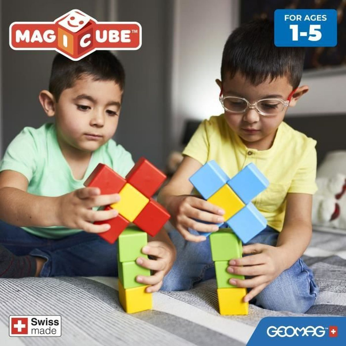 Due bambini giocano con blocchi magnetici colorati. Uno tiene rosso e giallo, l'altro blu e giallo. Sono su un letto.