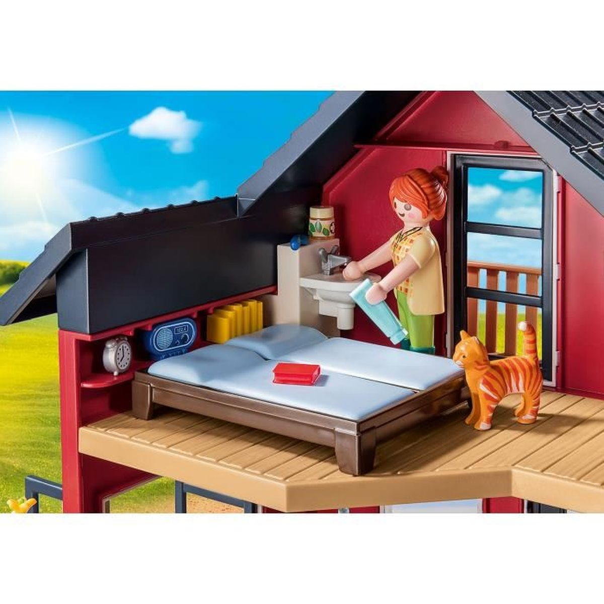 Eine Playmobil-Szene zeigt eine Frau mit roten Haaren in der Nähe eines Bettes, eines Waschbeckens und einer Katze. Die Szene spielt in einem roten Haus mit blauem Himmel.