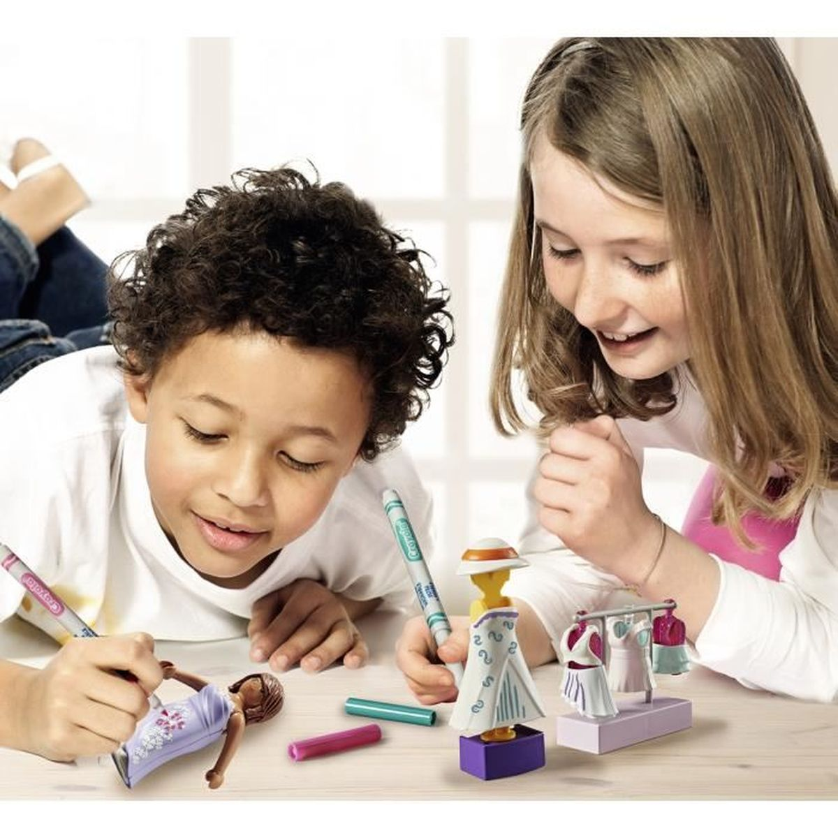 Zwei Kinder malen mit Markern auf Spielzeug. Ein Junge malt auf eine Puppe, und ein Mädchen schaut zu. Spielzeug und Marker liegen auf dem Tisch.