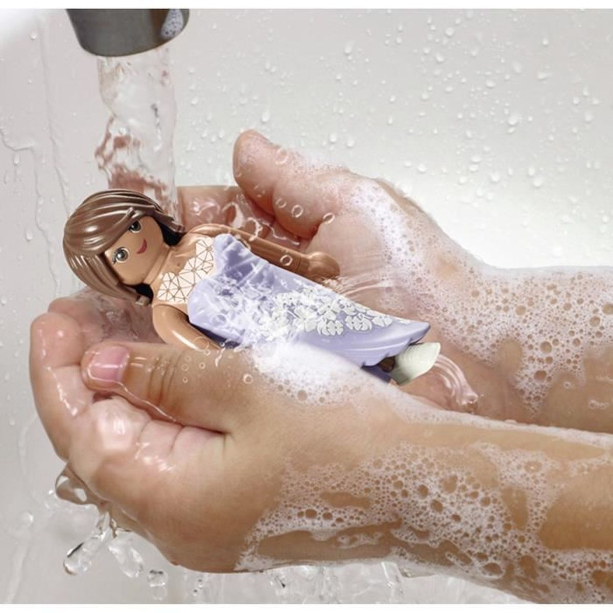 Eine Puppe wird in seifigen Händen unter fließendem Wasser gehalten. Die Puppe ist in eine hellviolette Decke mit weißen Mustern gehüllt.
