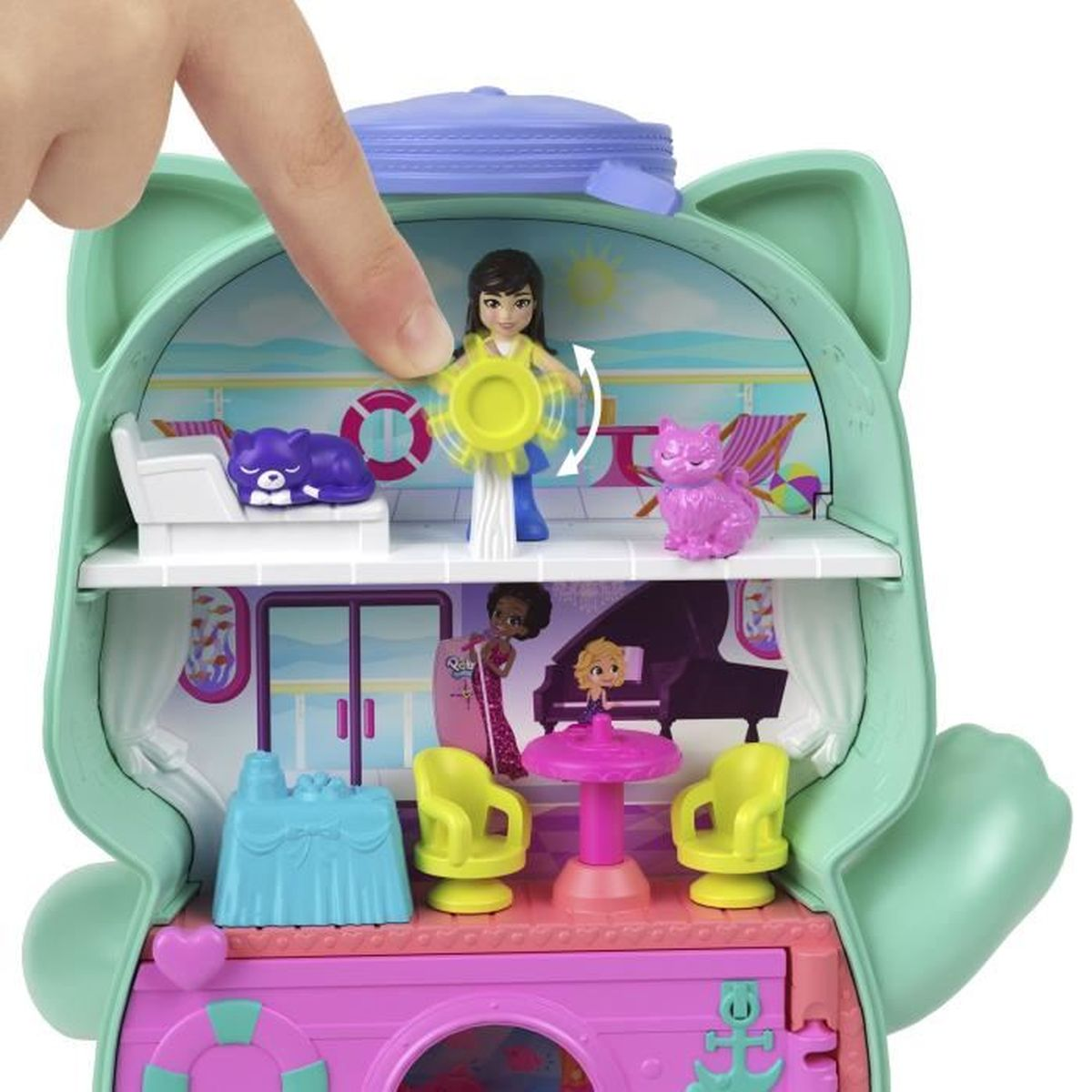 Een hand draait een geel speeltje in een katvormige speelset. Binnenin zijn poppen, een paarse kat, een piano en meubels. Roze, blauw en geel.