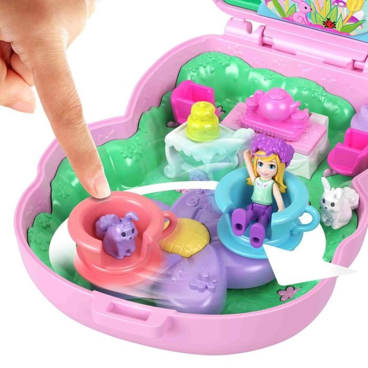 Eine Hand zeigt auf ein rosa Spielzeug-Teeparty-Set. Im Inneren befinden sich Puppen, Tiere und Möbel. Das Set ist rosa und lila.