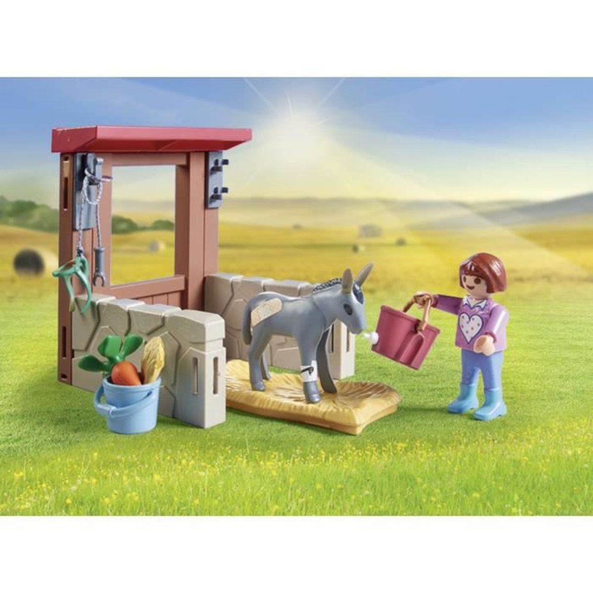 Una scena giocattolo mostra un asino in una stalla, una persona con un secchio e un secchio di verdure. Lo sfondo mostra un campo soleggiato.