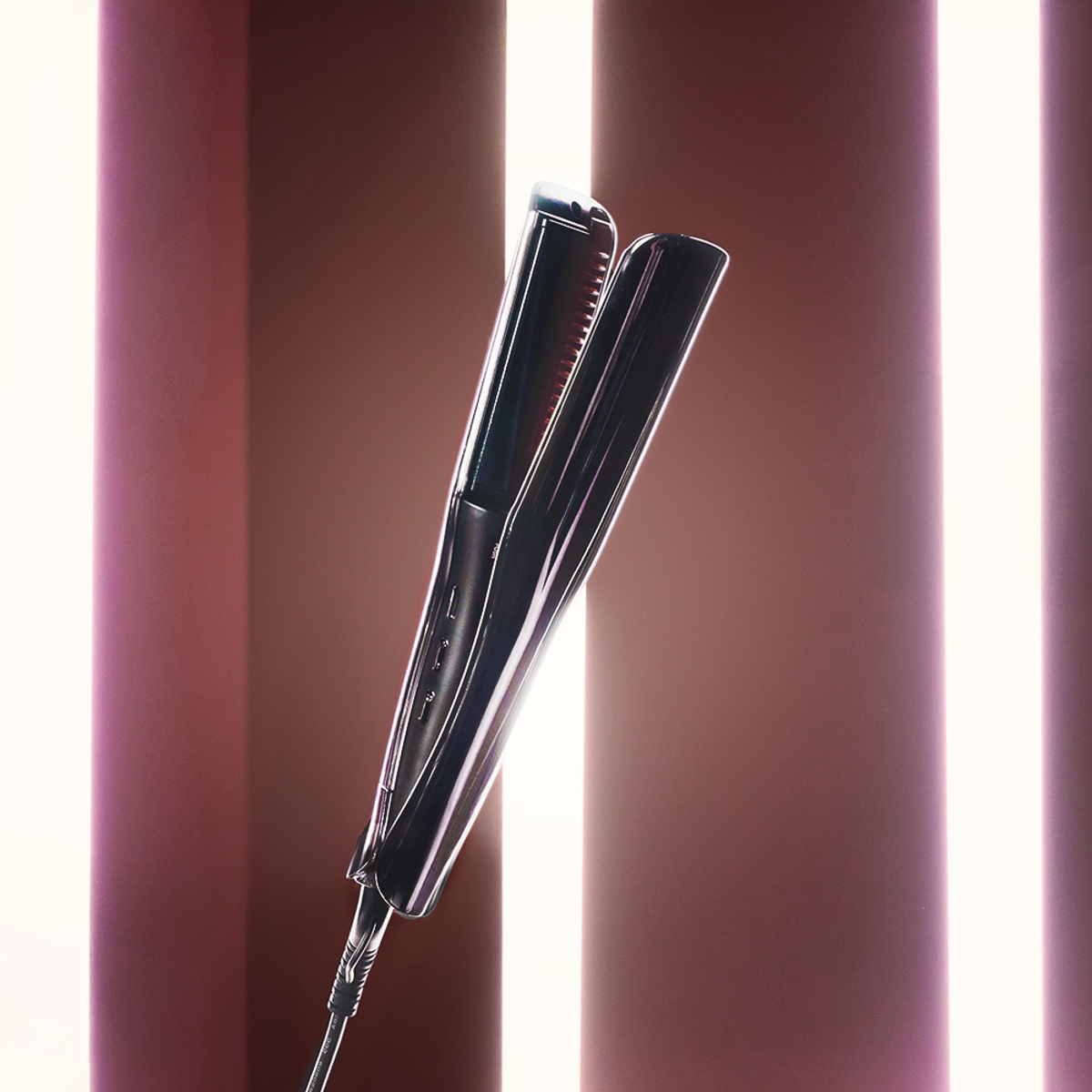 Una piastra per capelli nera con cavo è posizionata davanti a uno sfondo con strisce verticali rosa chiaro e scuro.