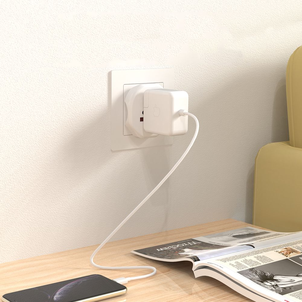 Witte voedingsadapter aangesloten. Een telefoon laadt op een houten tafel, naast een open tijdschrift.