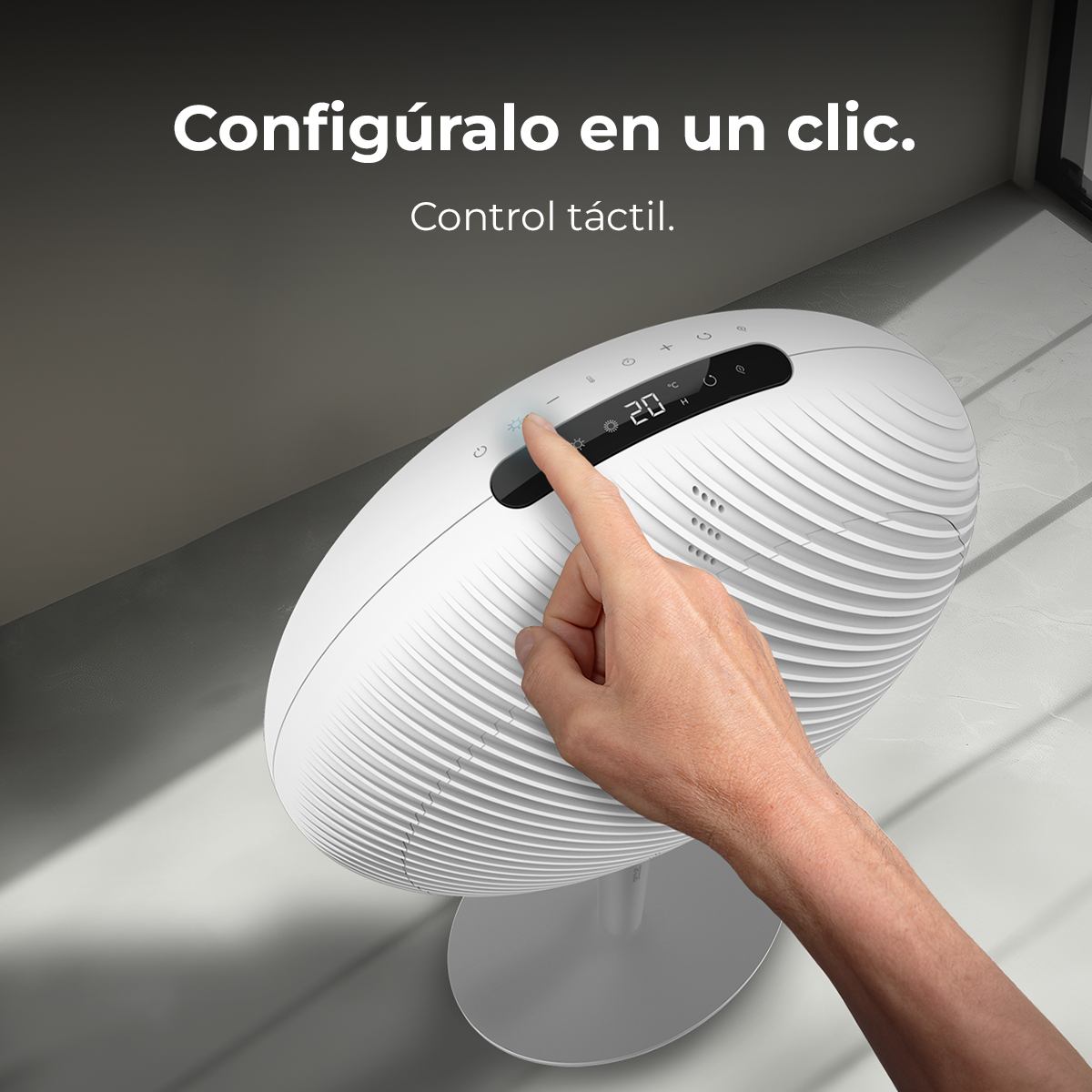 Una mano tocca il pannello di controllo di un ventilatore bianco. Il pannello mostra la temperatura e le impostazioni. Lo sfondo è un muro e un pavimento grigi.
