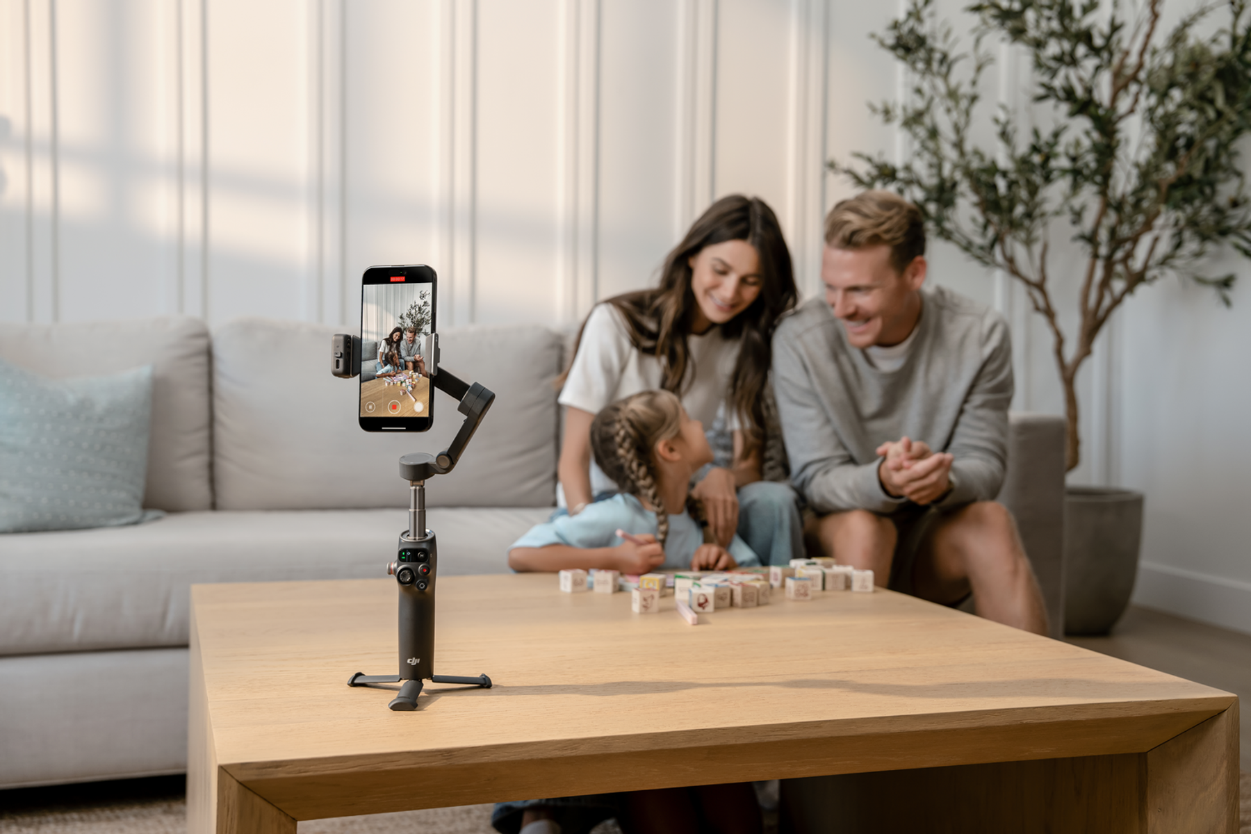 Rodzina nagrywa wideo smartfonem na statywie. Siedzą na kanapie w pobliżu stołu z drewnianymi klockami.