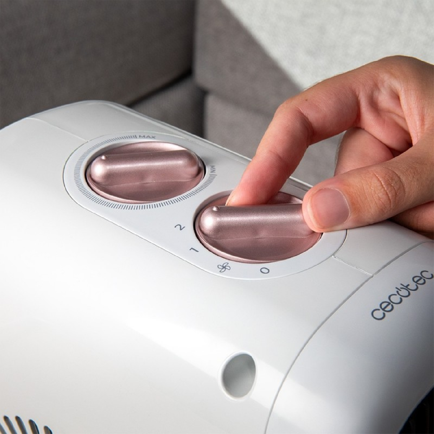 Una mano ruota un quadrante su un elettrodomestico bianco con dettagli oro rosa. Il quadrante ha impostazioni da 0 a 2 e un simbolo di ventola.