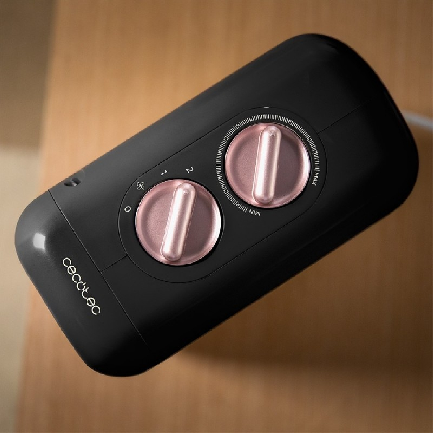 Un ventilatore nero con due quadranti e manopole di controllo rosa, posto su una superficie di legno.