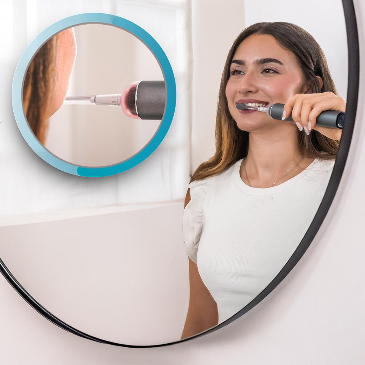 Donna che si lava i denti con uno spazzolino elettrico davanti a uno specchio. Specchio rotondo con riflesso incorniciato in blu.