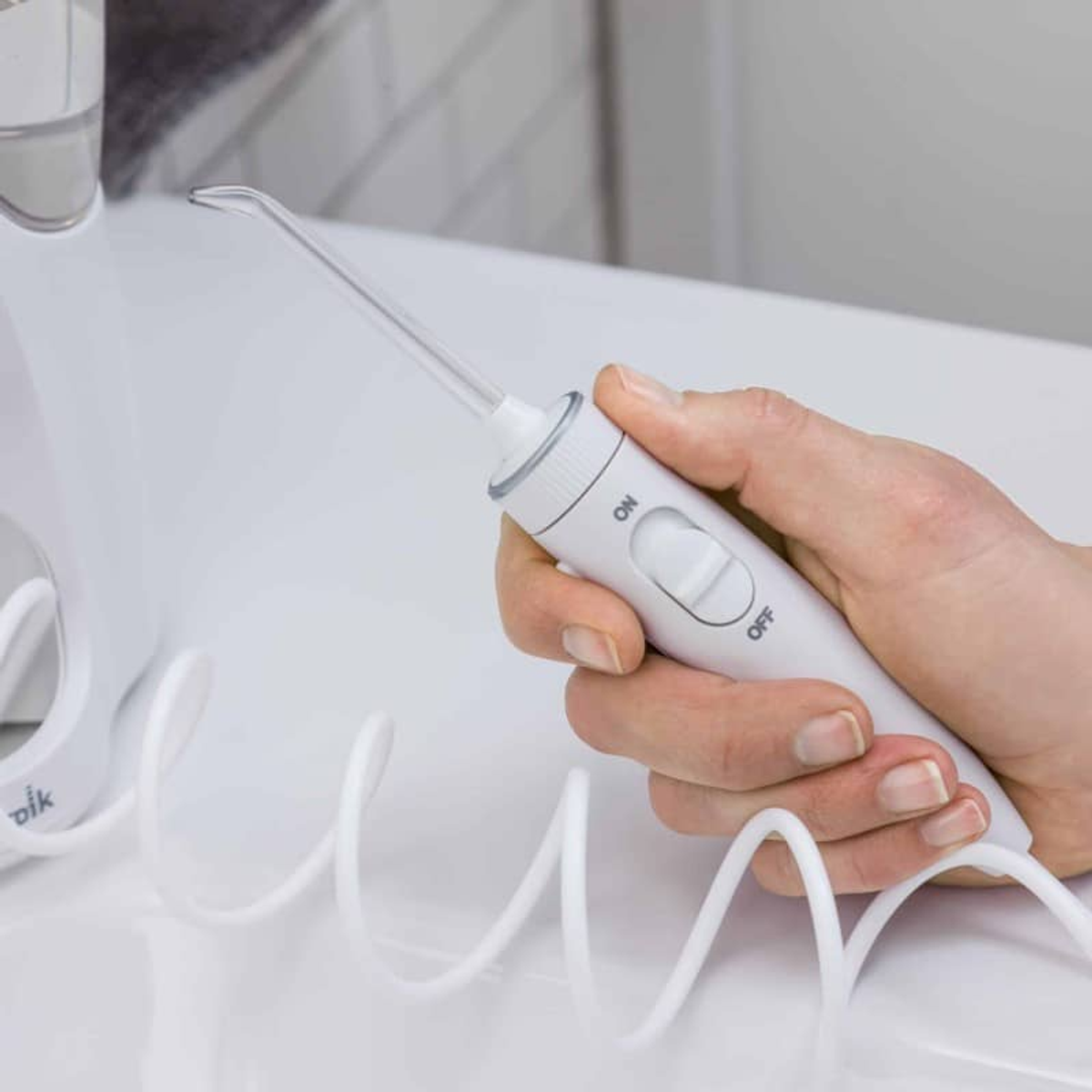 Una mano tiene un idropulsore bianco. È su una superficie bianca con un tubo bianco a spirale.