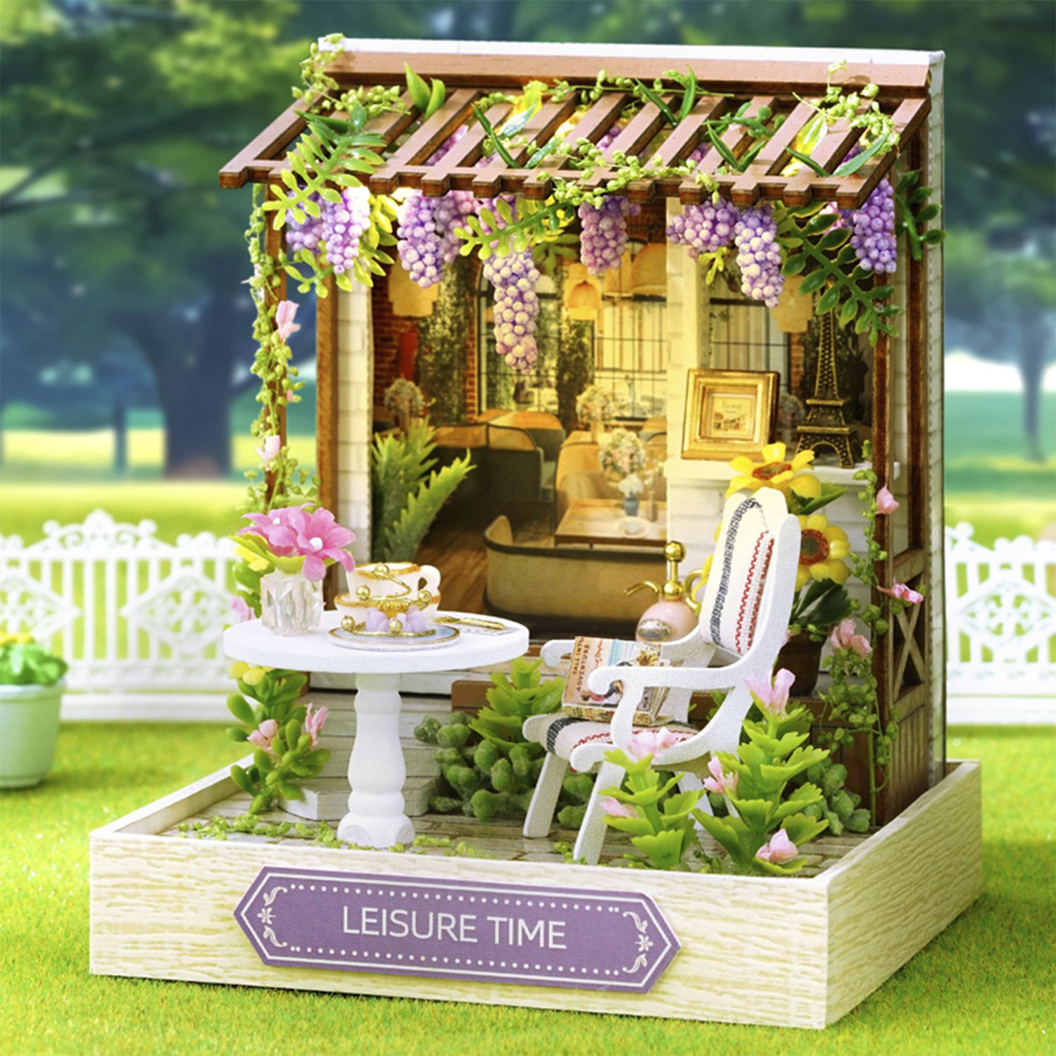Una scena di giardino in miniatura con sedia bianca, tavolo, fiori e pergola con viti e uva.