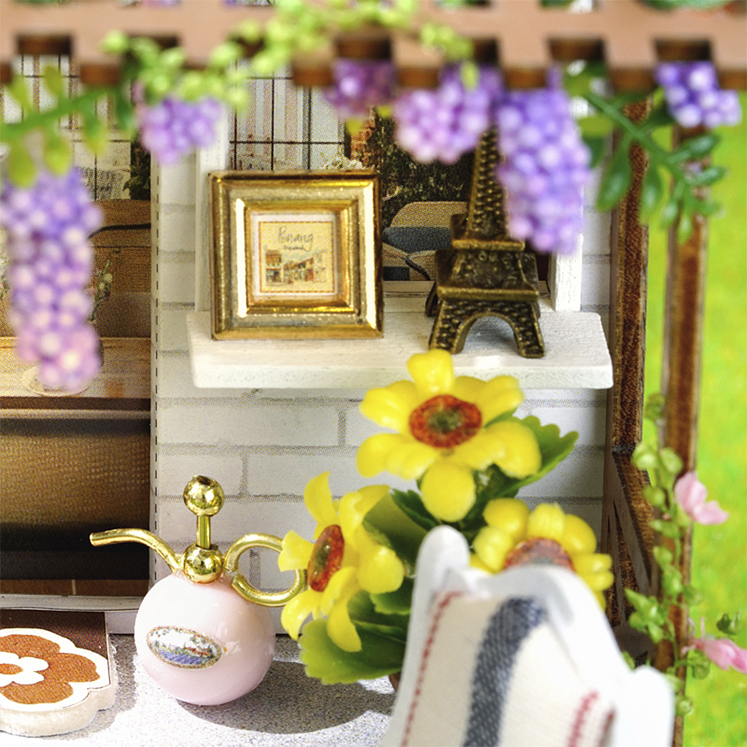 Scena in miniatura con fiori, Torre Eiffel e un'immagine incorniciata. Annaffiatoio rosa e sedia bianca in primo piano.