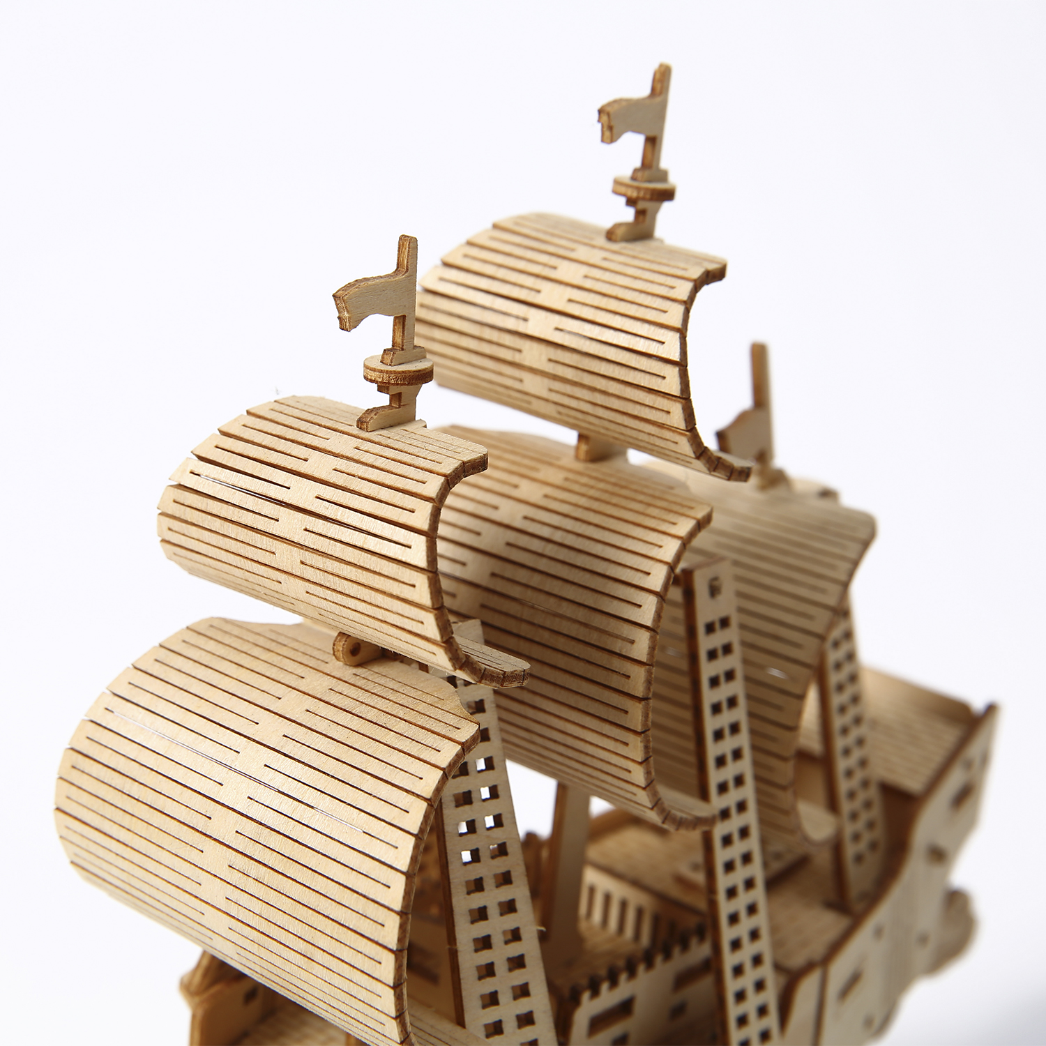 È mostrato un modello di nave in legno. Ha vele e alberi di legno dettagliati, con sfondo bianco. La nave è realizzata in legno marrone chiaro.