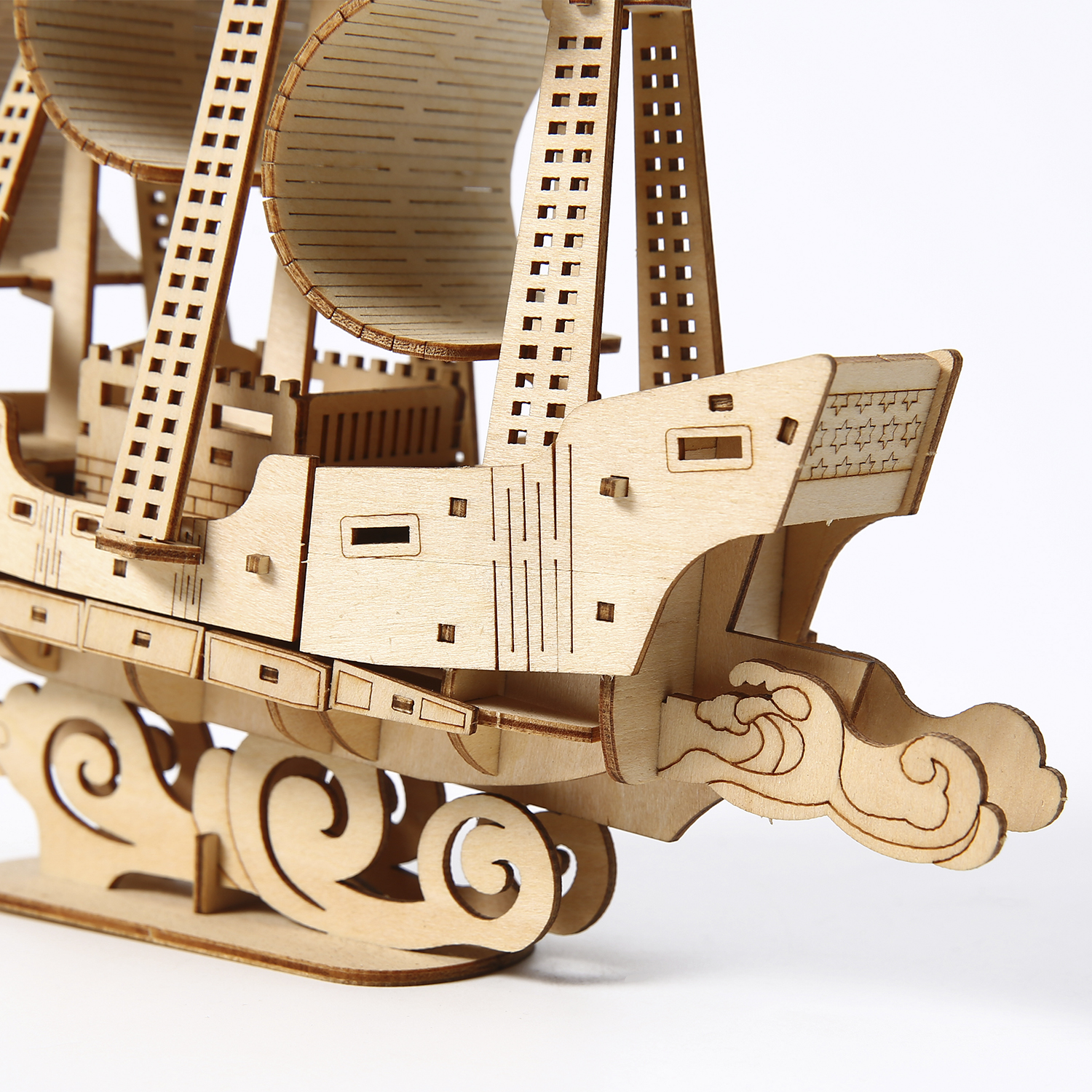 Un modello di nave in legno con vele e onde decorative su sfondo bianco. La nave è in legno marrone chiaro.