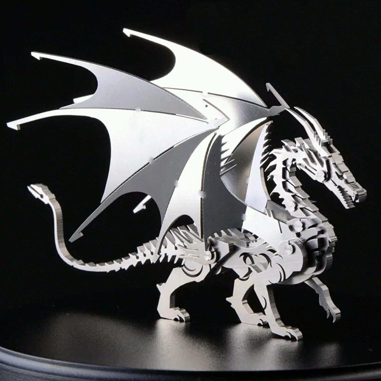Una scultura di drago in metallo con ali si erge su uno sfondo nero. Il drago ha scaglie e strutture alari dettagliate.
