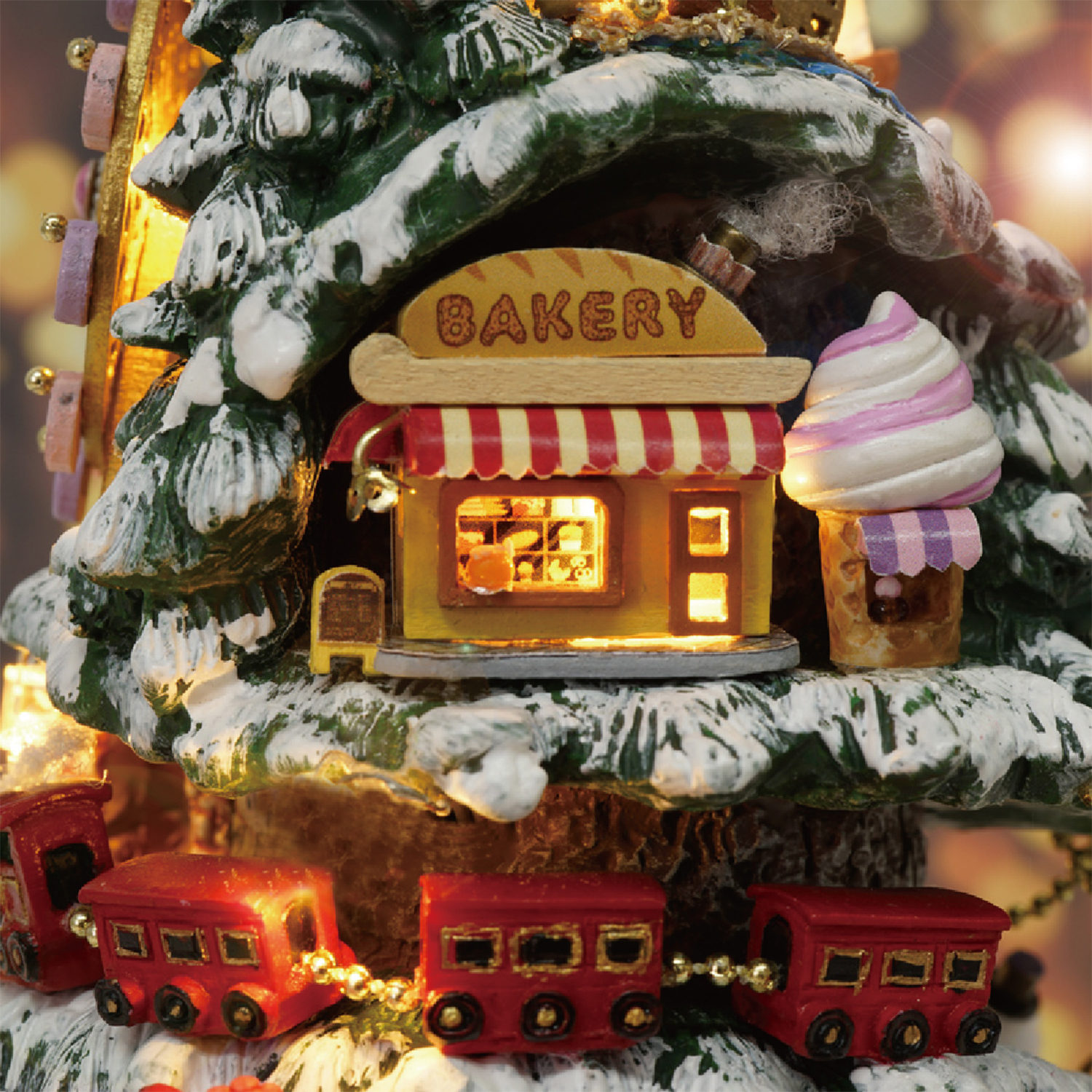 Una scena natalizia in miniatura con una panetteria, un gelato, un treno e un albero di Natale innevato.