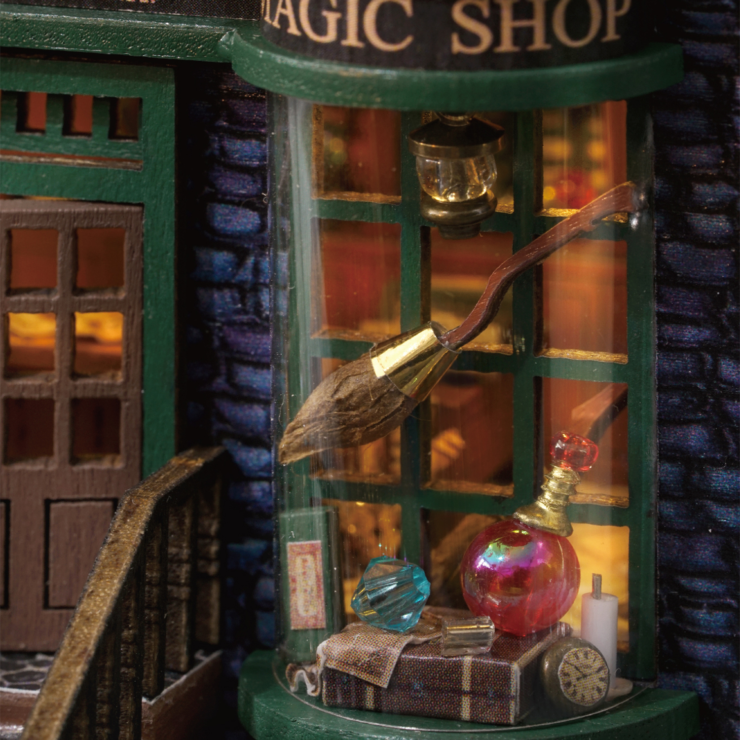 Ein Miniatur-Zauberladen mit einem Besen, einer Flaschen- und einer Uhr in einer Glasvitrine. Der Laden hat ein grünes und blaues Äußeres.