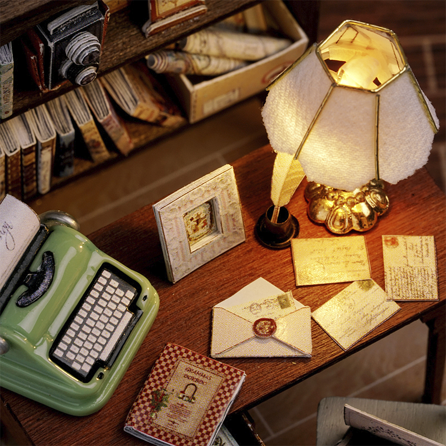 Scena di scrivania in miniatura con macchina da scrivere verde, lampada, libri, lettere e fotocamera su una mensola di legno.