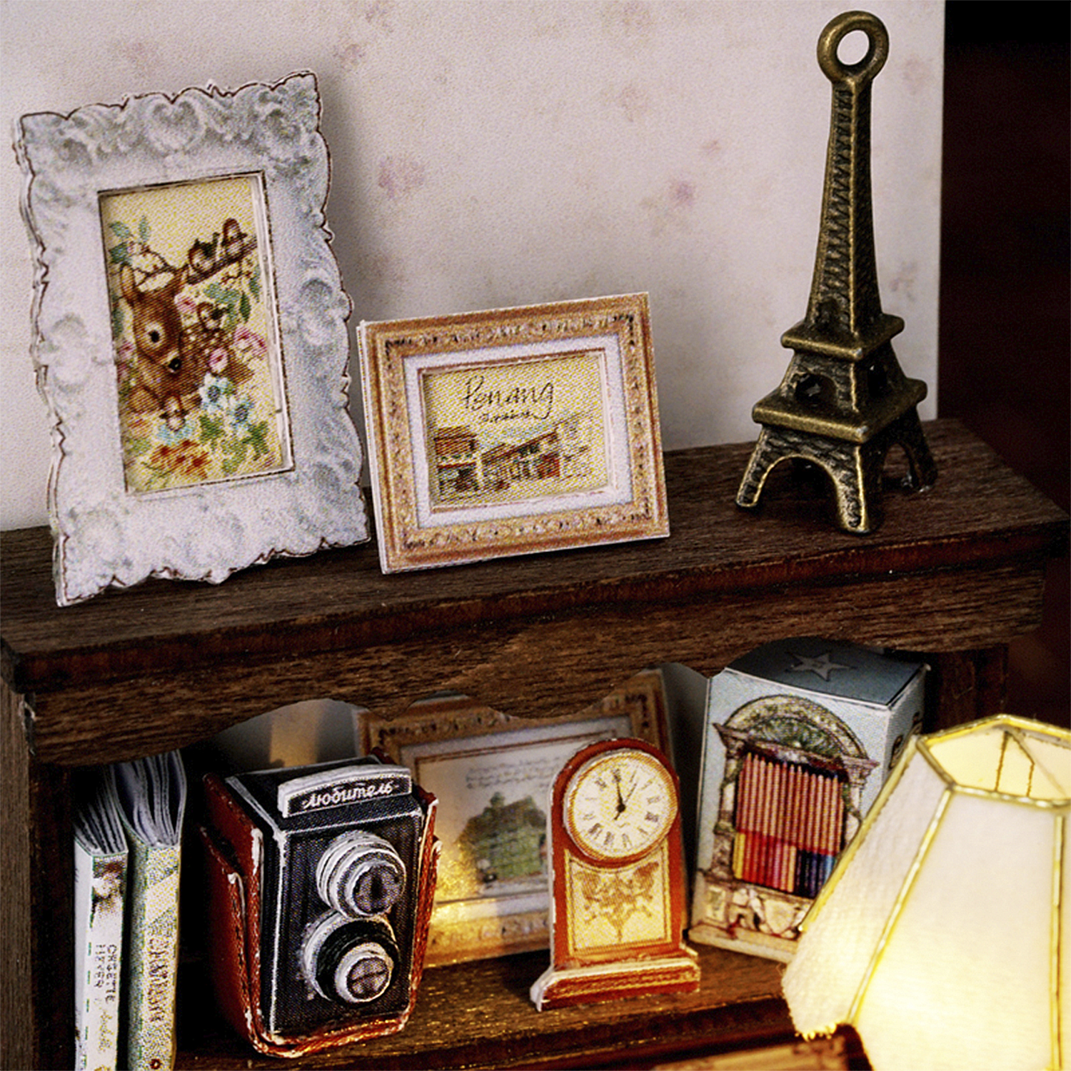 Stanza in miniatura con immagine di cervo, Torre Eiffel, macchina fotografica, orologio e lampada su scaffali di legno. Libri sotto.