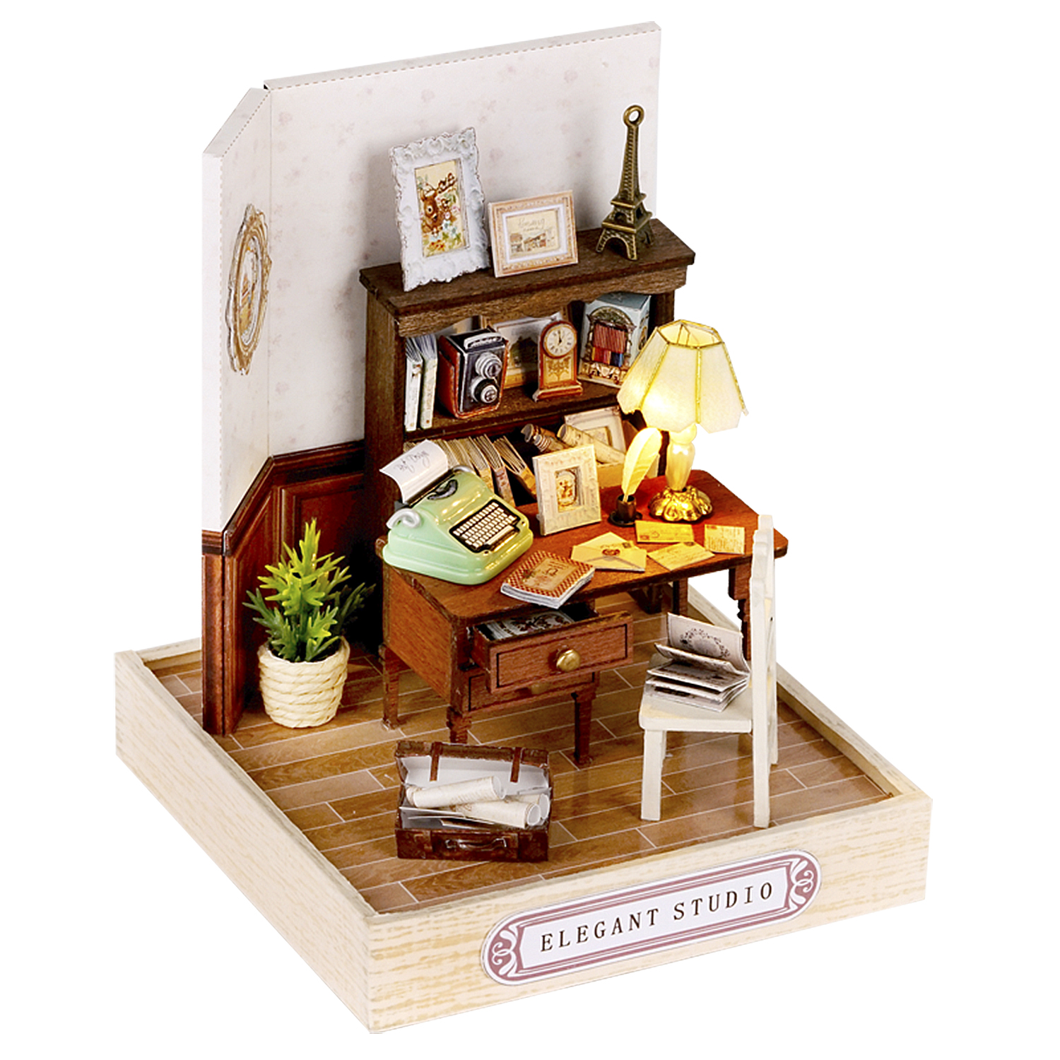 Scena di studio in miniatura con scrivania, macchina da scrivere, lampada, libri e modello della Torre Eiffel. Cornice in legno con testo 'Elegant Studio'.