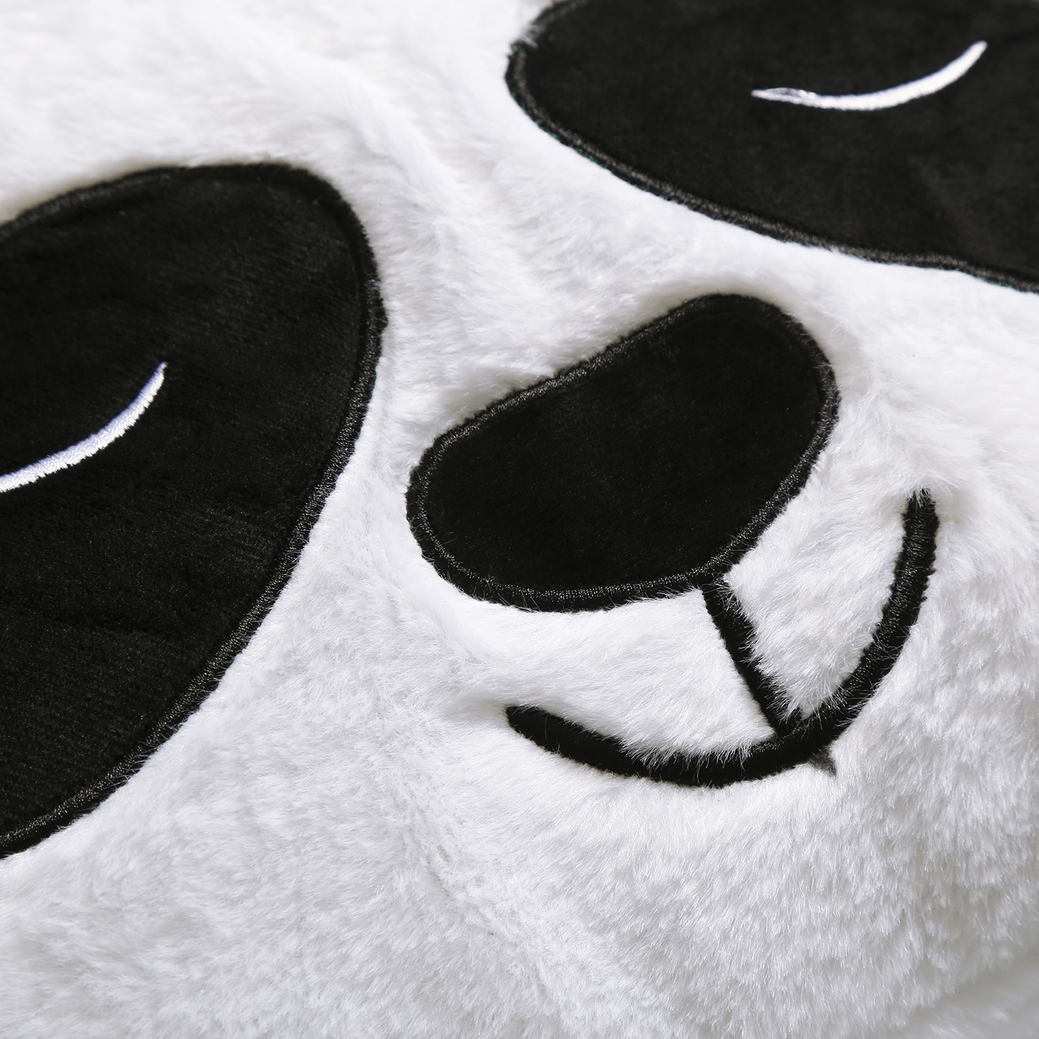 Primo piano di un volto di panda. Occhi e orecchie neri su materiale bianco e soffice. Bocca sorridente. Dettagli di cucitura bianchi.