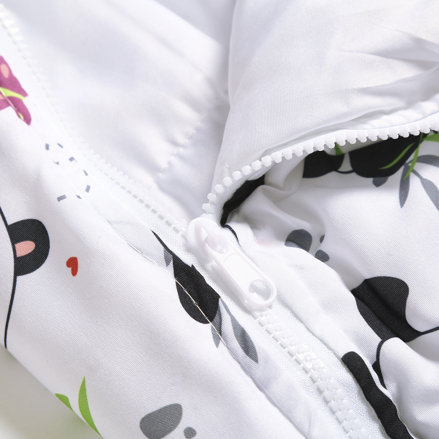 Primo piano di una giacca bianca con cerniera. La giacca ha una stampa floreale e panda con dettagli neri, rosa e grigi. La cerniera è bianca.