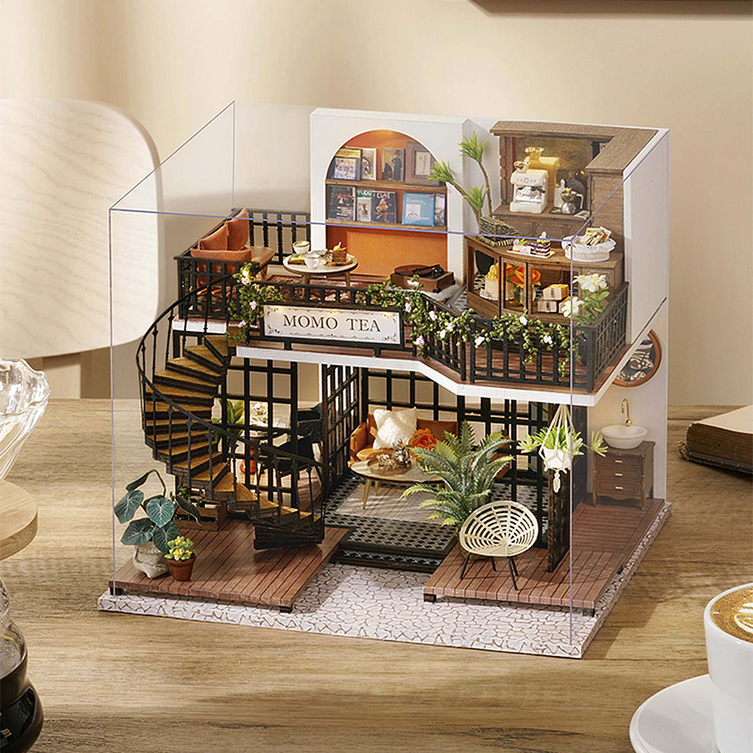 Un modello in miniatura del negozio Momo Tea con due piani, scala a chiocciola e decorazioni interne dettagliate. È su un tavolo di legno.