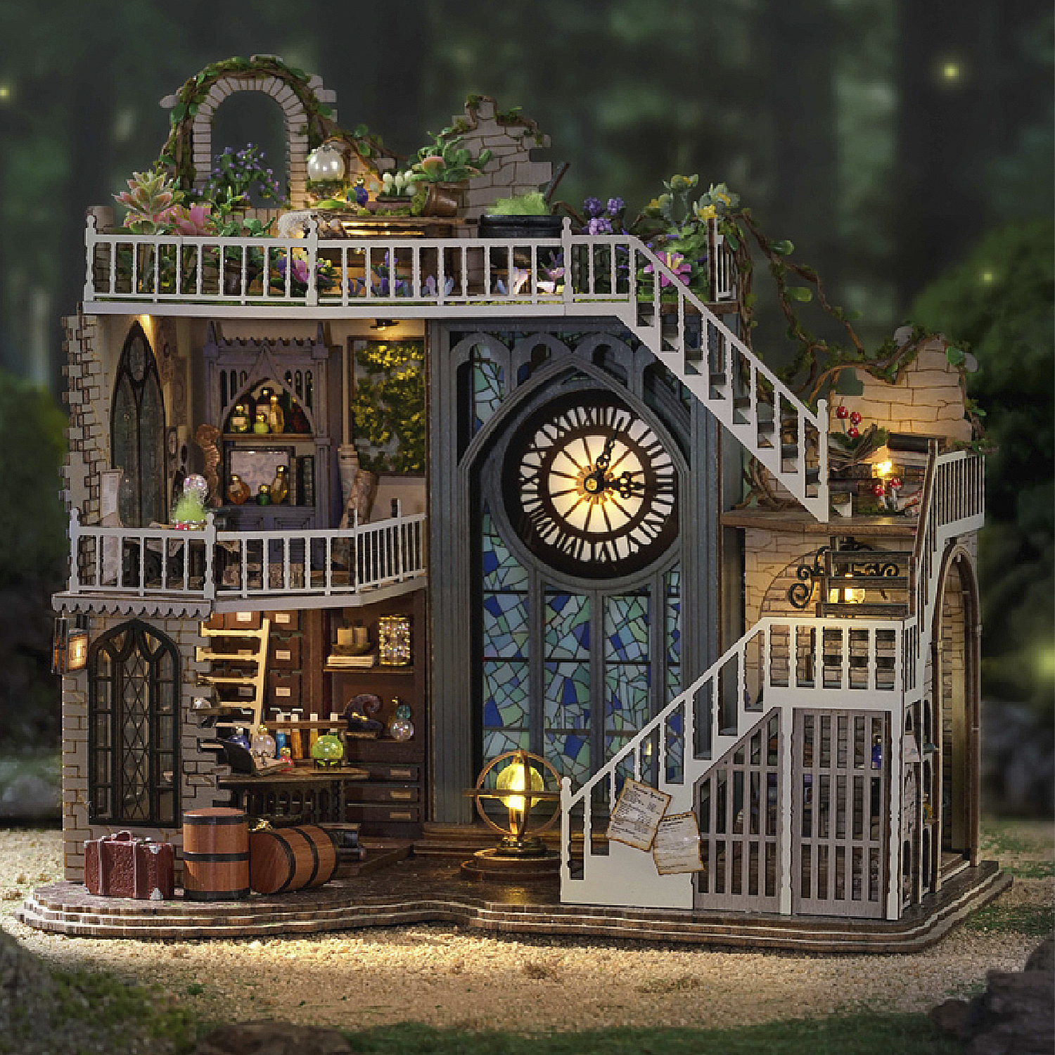 Una casa in miniatura dettagliata con scale, un orologio e vetrate colorate. Ha un balcone con piante ed è illuminata. Botti e bagagli davanti.
