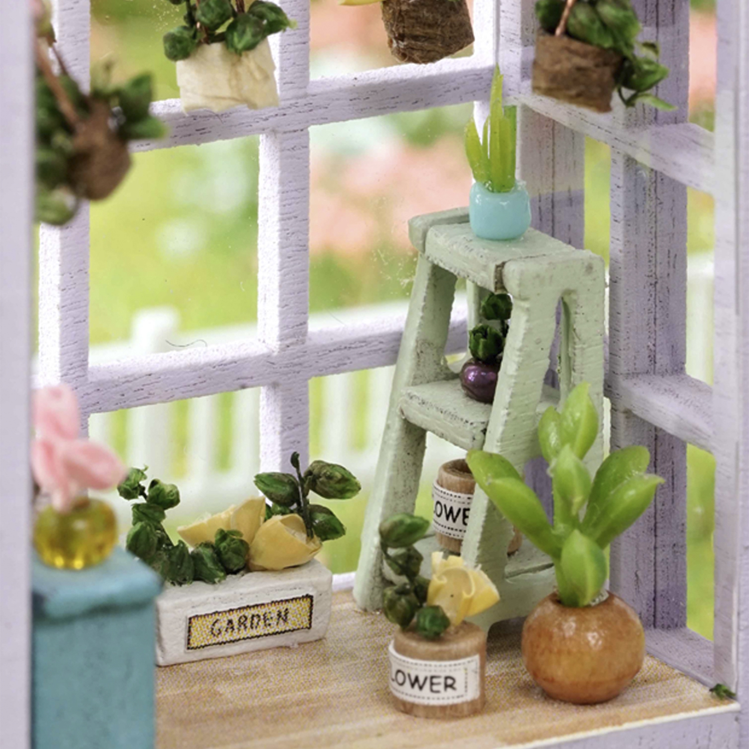 Scena di giardino in miniatura con piante in vaso, una piccola scala e un telaio di finestra. La scena è illuminata dalla luce naturale.