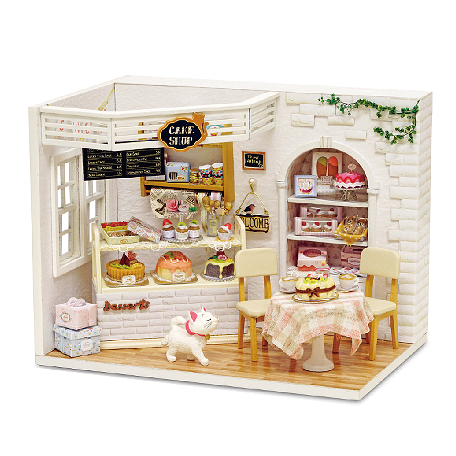 Ein Miniatur-Kuchenladen mit Kuchen, einer Katzenfigur, Tischen und Stühlen. Auf dem Schild steht 'Cake Shop' und 'Welcome'.