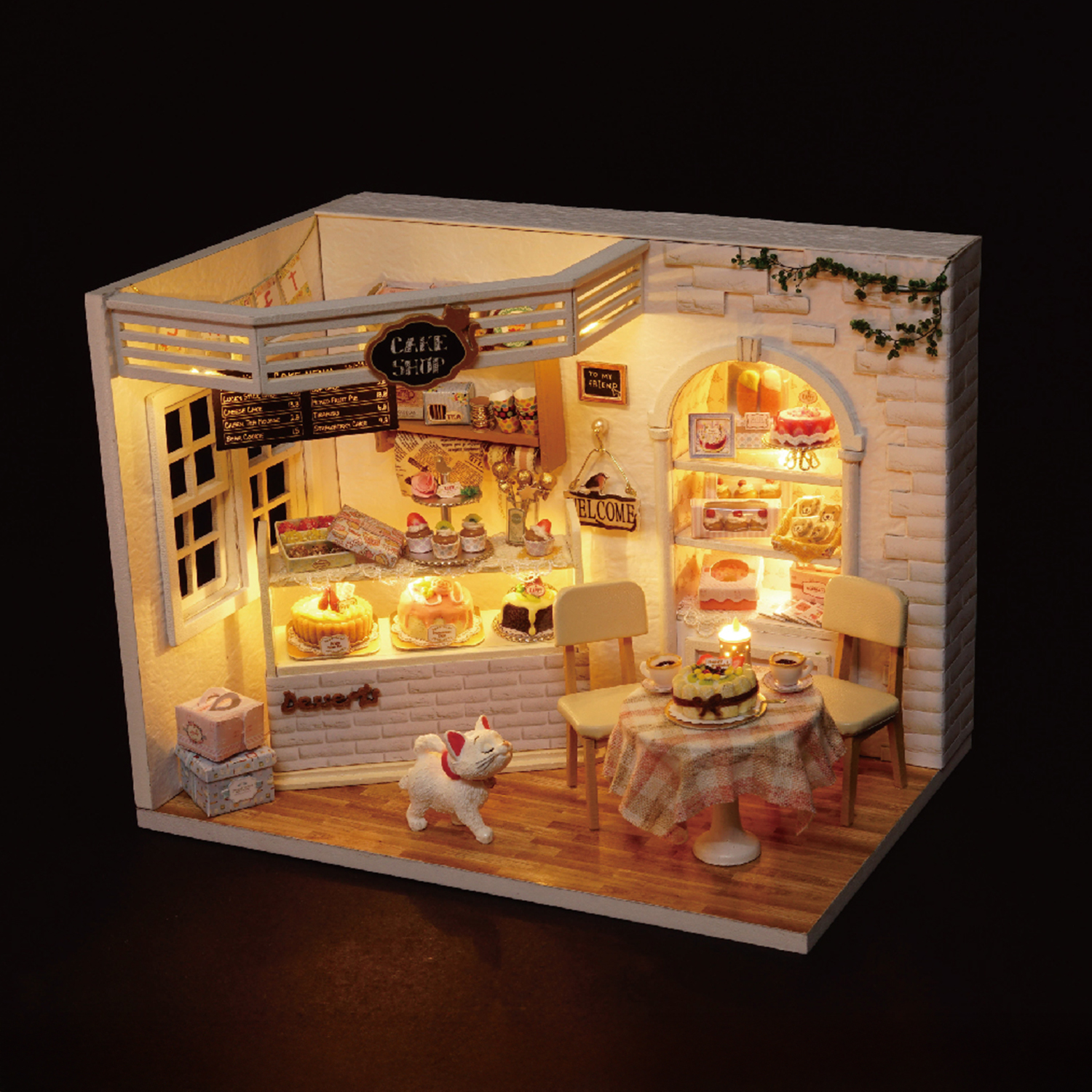 Ein Miniatur-Kuchenladen mit Kuchen, Tischen, Stühlen und einer Katzenfigur. Warme Beleuchtung schafft eine gemütliche Atmosphäre.