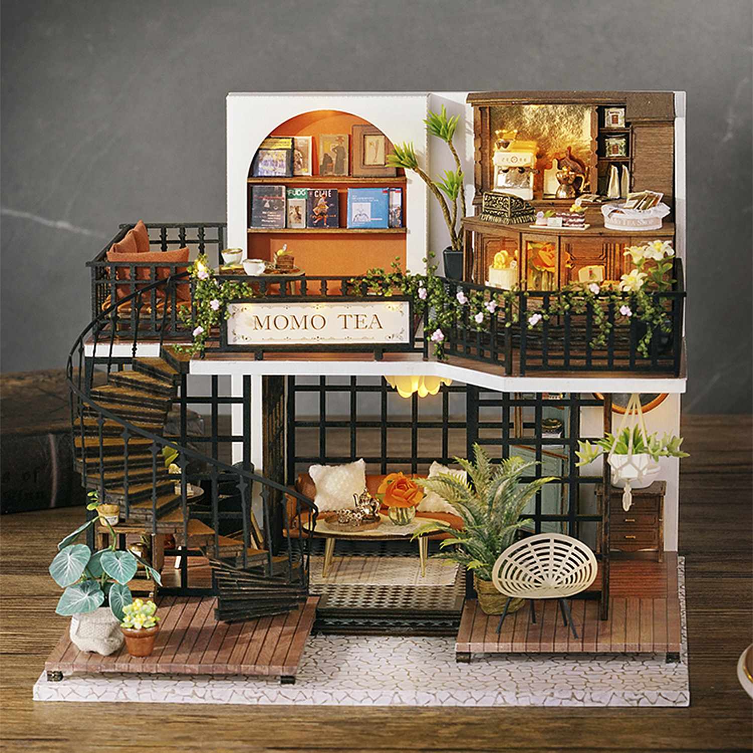 Casa in miniatura con interni dettagliati. Include scala a chiocciola, piccoli mobili, piante e insegna 'MOMO TEA'. Struttura a due piani.