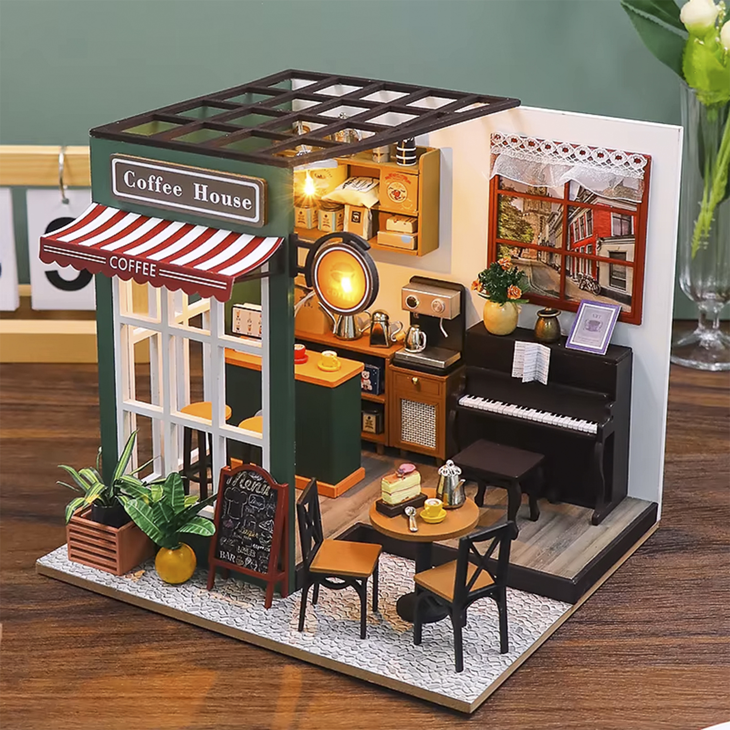 Caffè in miniatura con tenda a strisce rosse, pianoforte e tavolini con sedie. I dettagli includono piante e una lavagna del menu.
