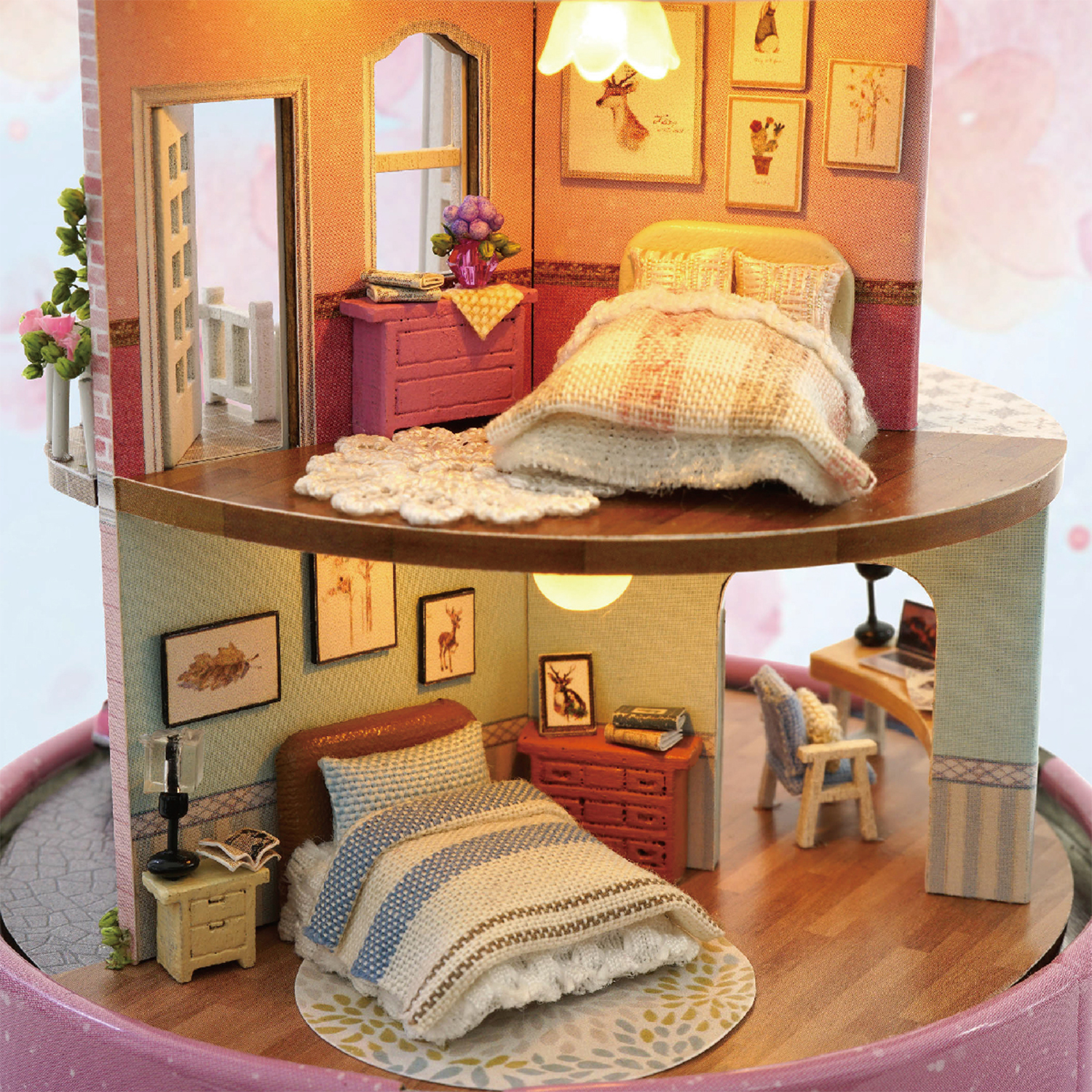 Una casa delle bambole a due piani con camere da letto. Il piano superiore ha un letto e delle immagini. Il piano inferiore mostra un altro letto, una scrivania e una lampada.