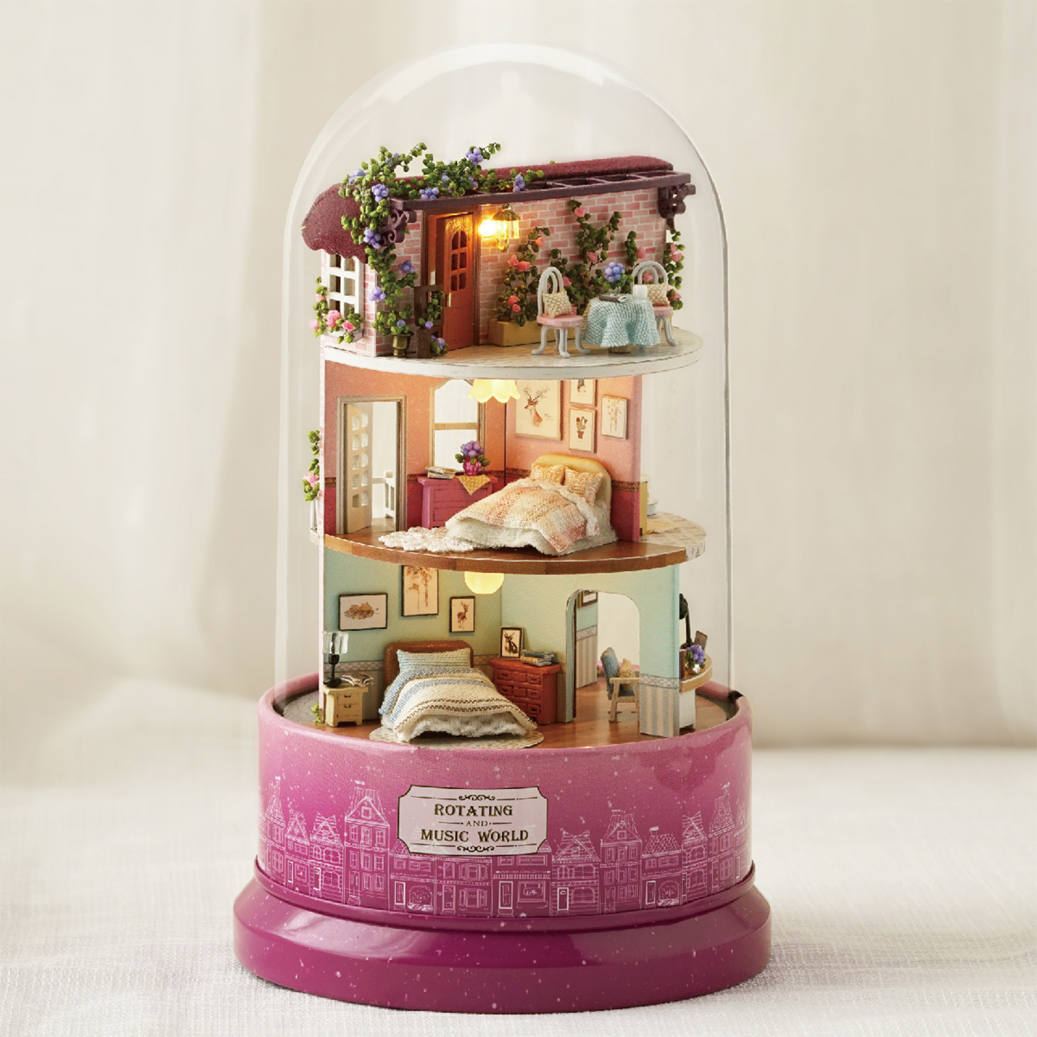 Una casa delle bambole in miniatura in una cupola di vetro. Ha tre piani con mobili e una base rosa rotante. Il piano superiore ha un patio.